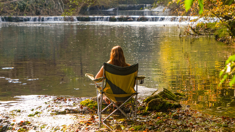 A woman sitting in a camping chair looking at a lake